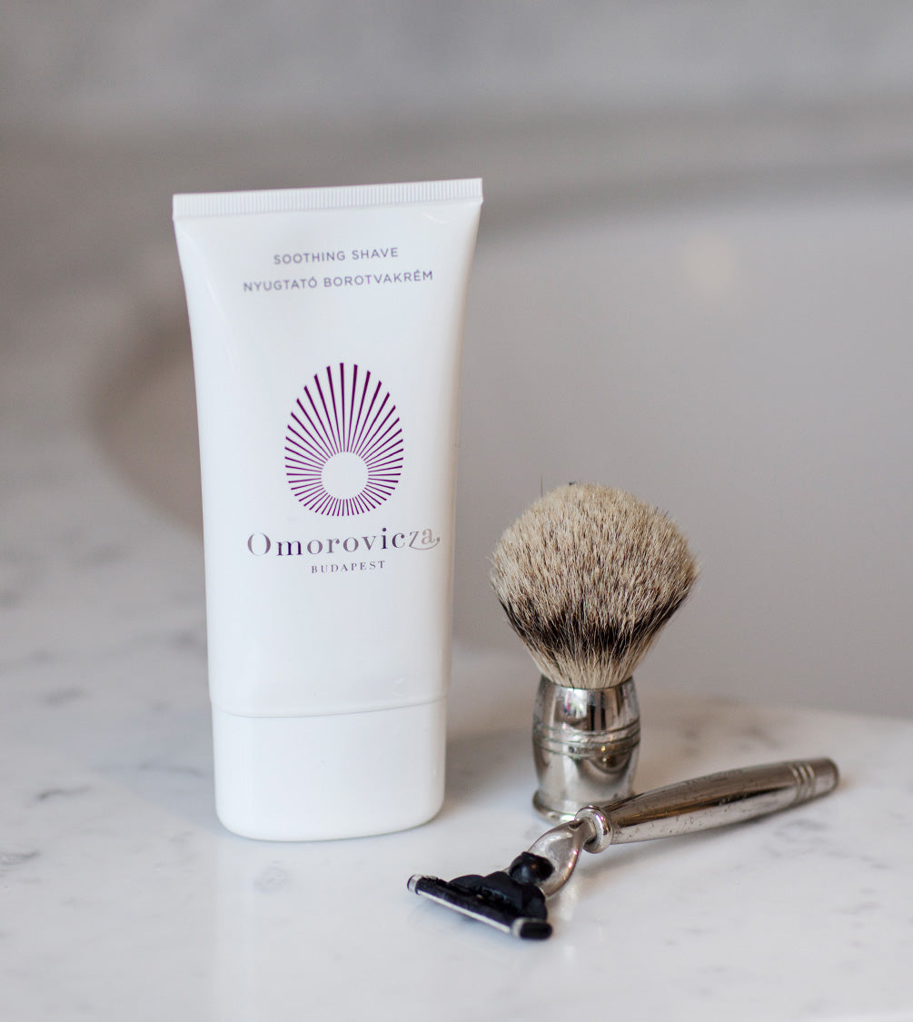 A tube of Soothing Shave next to shaving brush and razor on top of the sink.