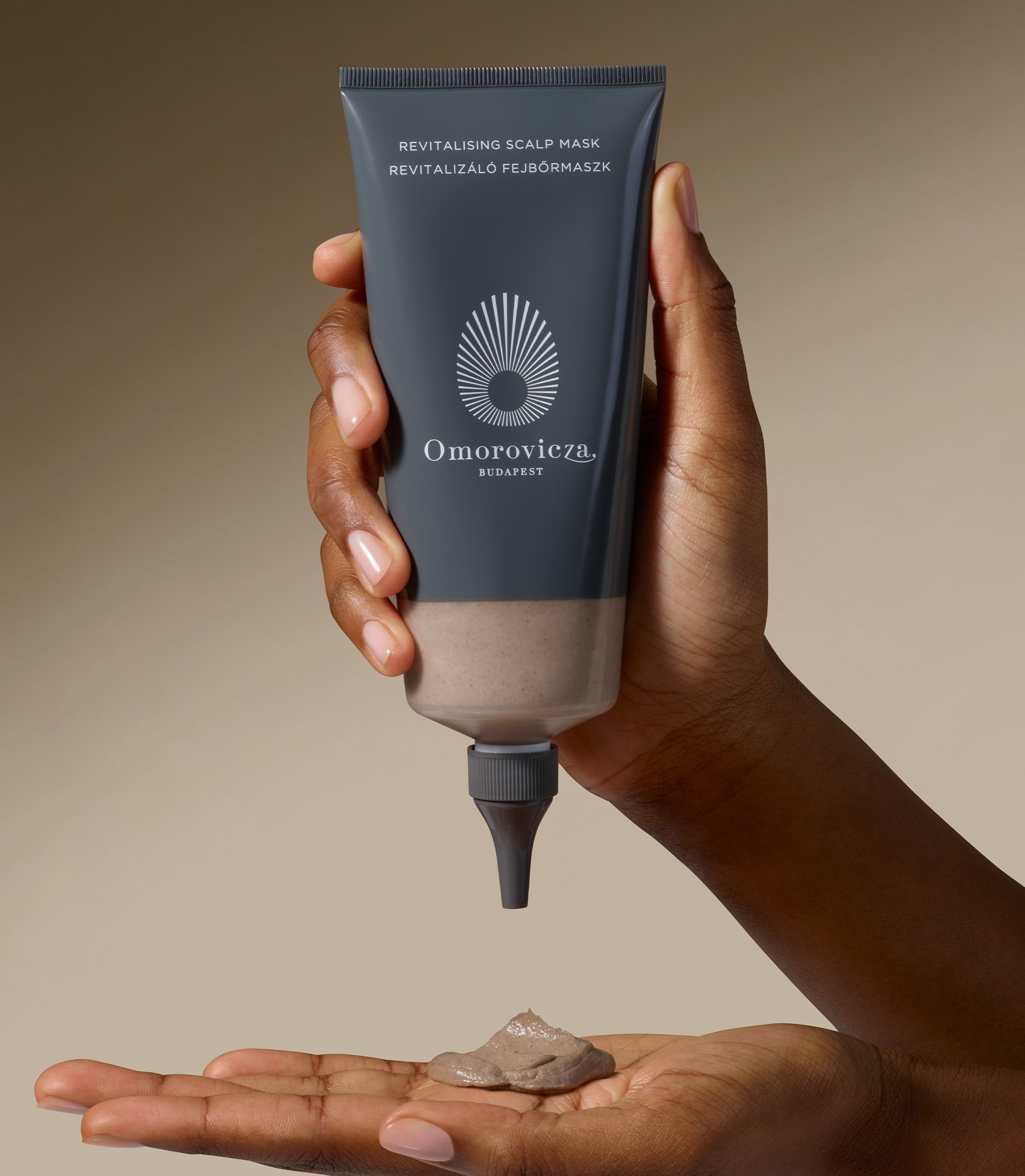 A hand is holding Revitalising Scalp Mask. A plum size of the product is in another hand