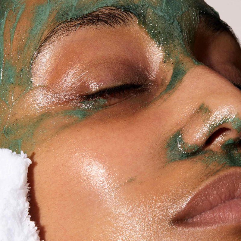 A close up of models face using a white mitt to clean a face mask of her face.